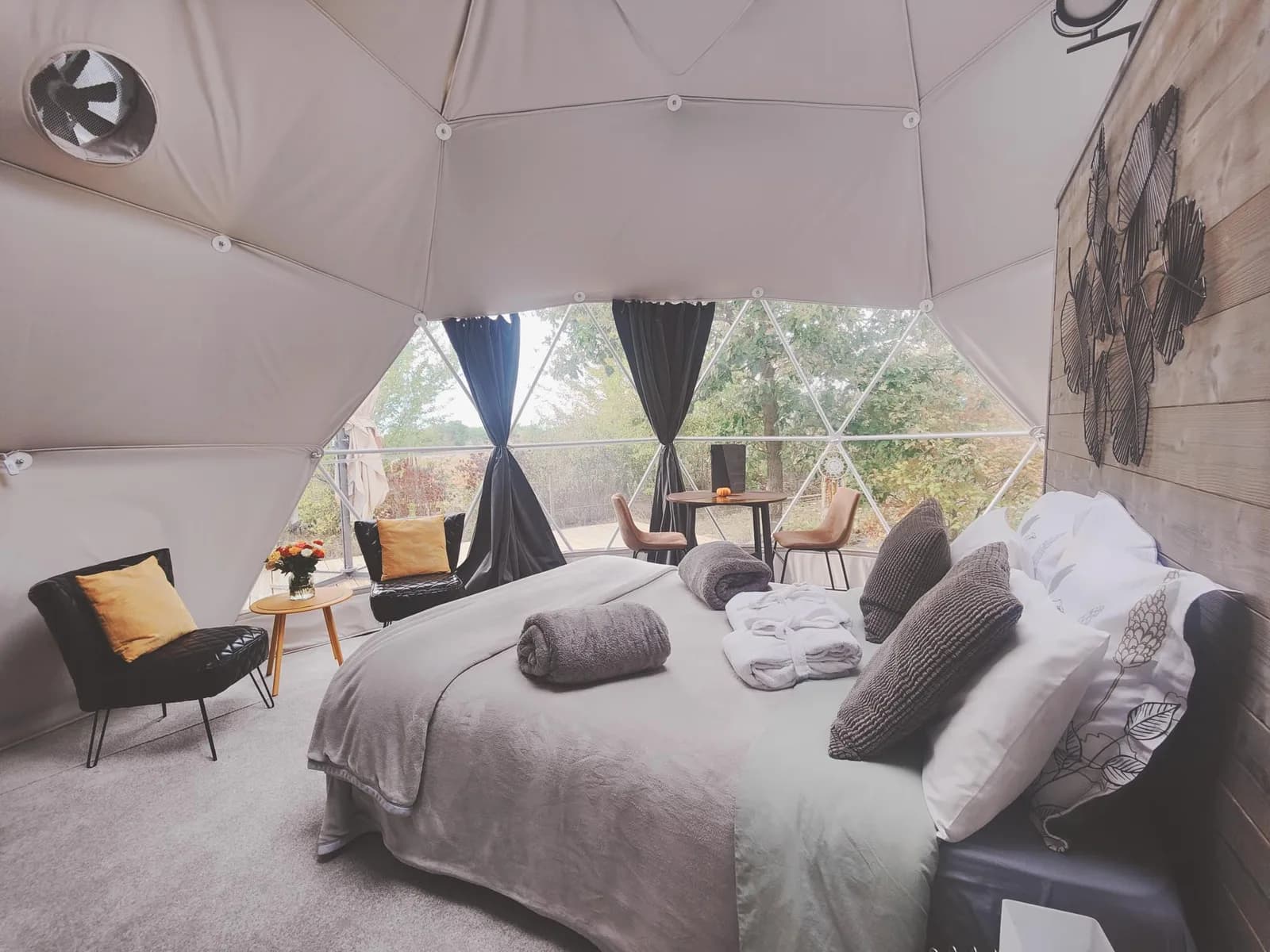 Intérieur d'un COCOON : lit double face à la baie panoramique ouverte sur les arbres